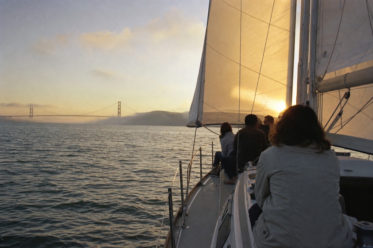 The Bay Bridge lights strung in a long curve across dark water, seen low from the deck of a boat on a clear evening.